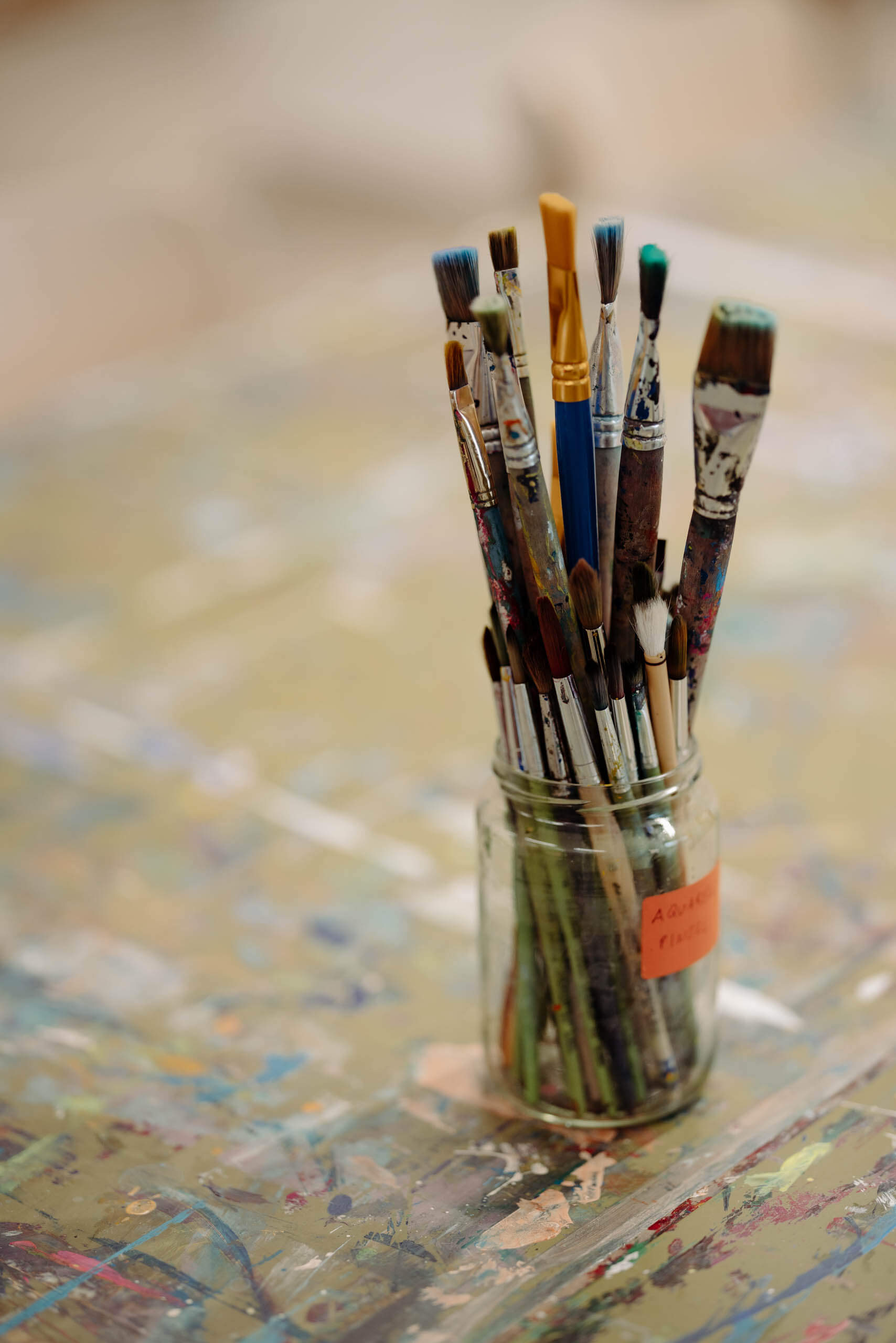 Ein Glas voller bunter Pinsel auf einem Maltisch im Atelier M7.
