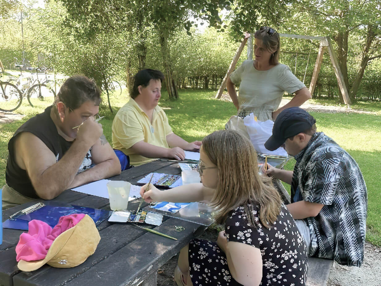 Teilnehmende malen im Donnenbergpark auf einer Parkbank im Rahmen eines Outdoor-Kunstworkshops im M7.